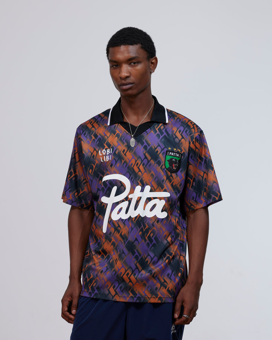 Model wearing the Patta All Over P Football Jersey in pansy purple and orange with script logo.
