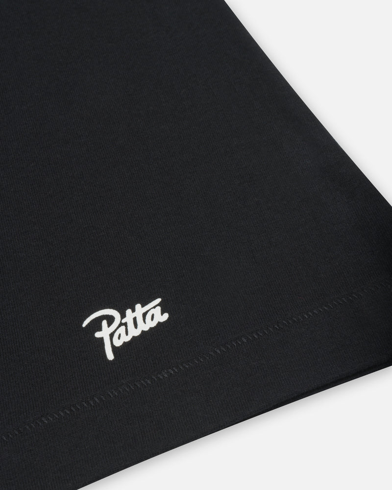 Close-up of the white Patta Script logo printed above the bottom hem on a black cotton t-shirt.
